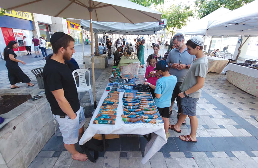 A family browsing the Friday Clal Building plaza market stops to check out some amazing olive wood and resin creations. (photo credit: NATAN ROTHSTEIN)