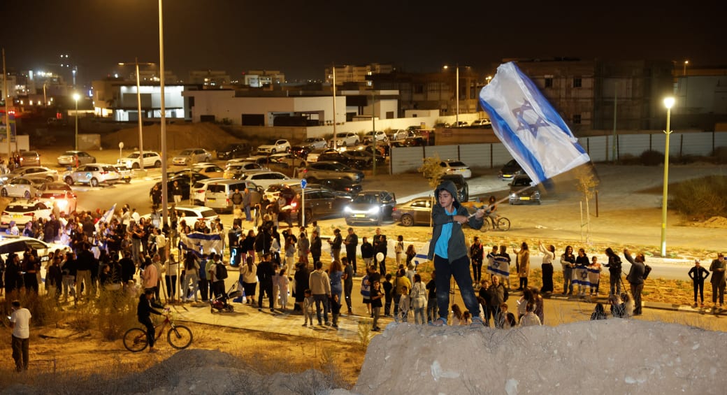  A boy waves an Israeli flag, as people wait for an expected convoy carrying newly released hostages that were seized during the October 7 attack by Palestinian militant group Hamas and held in the Gaza Strip, in Ofakim, Israel, November 26, 2023 (photo credit: REUTERS/AMIR COHEN)