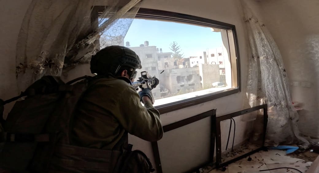  An Israeli soldier fires a weapon from a window during operations in the Gaza Strip amid the ongoing conflict between Israel and the Palestinian Islamist group Hamas, in this screen grab taken from a handout video released on December 4, 2023. (photo credit: REUTERS/IDF HANDOUT)