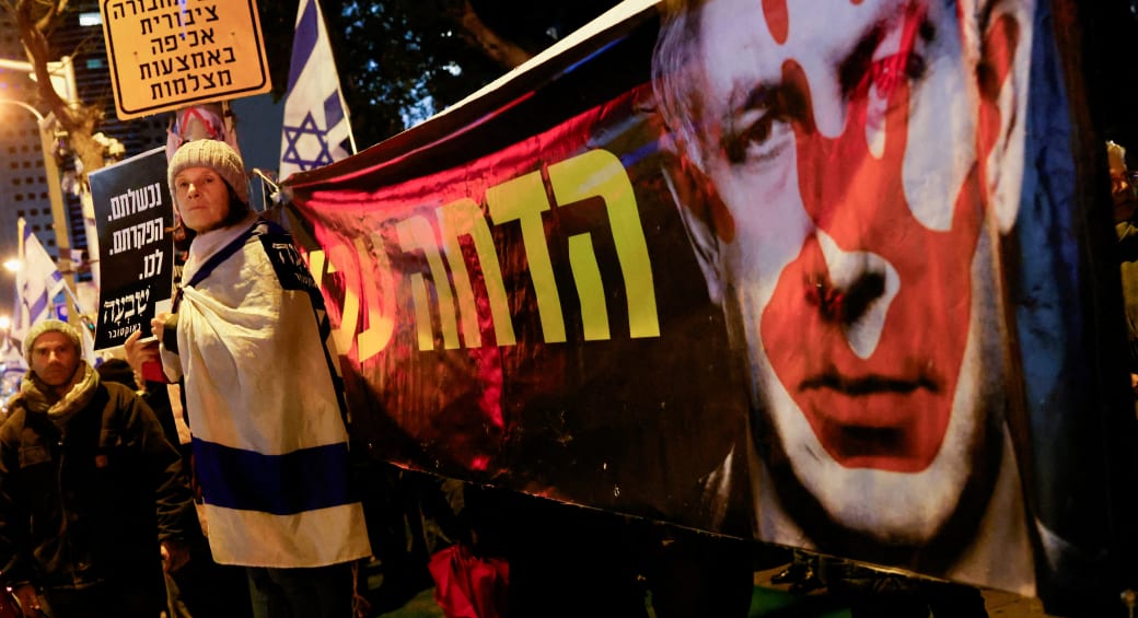  A demonstrator stands next to a banner with an image of Prime Minister Benjamin Netanyahu in Tel Aviv, Israel, January 27, 2024 (photo credit: REUTERS/TYRONE SIU)