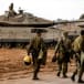 Israeli soldiers walk past Israeli tanks near Israel's border with the Gaza Strip, in southern Israel October 15, 2023.
