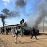  Palestinians react as an Israeli military vehicle burns after it was hit by Palestinian gunmen who infiltrated areas of southern Israel, at the Israeli side of Israel-Gaza border, October 7, 2023. 