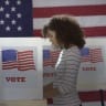  A woman in polling station, voting in a booth with US flag in background