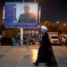 An Iranian cleric walks past a billboard depicting a portrait of the former commander of the IRGC Aerospace Forces, Brigadier General Amir Ali Hajizadeh, on February 21, 2026. 