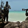 FILE PHOTO: Armed militiamen and a pirate walk on a rocky outcrop on the coast in the central Somali town of Hobyo as a a hijacked Korean supertanker lies anchored on the horizon on August 20, 2010.