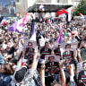 Protesters hold signs depitcting Jean-Luc Melenchon as in a mugshot and reading "Antisemite Populist, Jean-Luc Melenchon, Repeat offender, Puts a target in the back of Jews." 