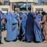 Afghan burqa-clad women queue to receive food aid from a local charity during the Islamic holy fasting month of Ramadan in Ghazni on February 24, 2026.