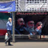 A man walks past Iran’s national flag and a banner bearing the images of the late founder of the Islamic Revolution, supreme leader Ayatollah Ruhollah Khomeini (R), the late Iranian supreme leader Ali Khamenei and his son, the current supreme leader Mojtaba Khamenei (L), in Tehran, June 10.