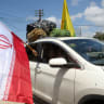 A displaced woman holds an Iranian national flag from the window of a vehicle, as she crosses the southern Lebanese area of al-Qasmiyeh, on her way back to her home village in southern Lebanon on June 15. 