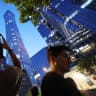 A man points a mobile phone at CITIC Tower, also known as China Zun, where damage is visible on a high floor of the exterior, in Beijing, China June 26, 2026. 