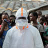 A health worker in personal protective equipment (PPE) stands near displaced people waiting for the burial of suspected Ebola victims at the Kigonze displaced persons camp, one month after an outbreak was declared, in Bunia, eastern Democratic Republic of Congo, June 18, 2026. 