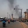 A column of black smoke rises above buildings as traffic passes the Africa Tower monument in Bamako on April 26, 2026. 