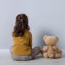 Little girl with teddy bear near light wall indoors, back view