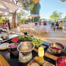 A vibrant, sun-drenched view of the open-air terrace at the Logos Hotel, where an expansive farm-to-table prep station loaded with fresh, raw ingredients sets the stage for Luiza’s monthly ‘Meshak Shuk’ culinary festival.