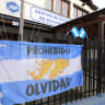 An Argentinian flag featuring a map of the Falkland Islands and a sign reading "Never Forget" is seen at the entrance of the Malvinas War Veterans Center, where fans watch the 2026 World Cup football semi-final match between Argentina and England on a television in Ushuaia, on July 15, 2026.