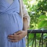 A pregnant woman is seen holding her stomach in front of foliage (illustrative)