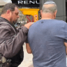 A police officer escorts a man away after appearing to smack the phone of MK Moshe Tur-Paz's aide, following a death threat towards a woman, July 24, 2026.