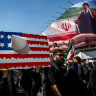 A person holds a placard representing a US flag, with an image of Iran's new Supreme Leader Mojtaba Khamenei on a billboard in the background, on the day of a ceremony marking 40 days since Ayatollah Ali Khamenei was killed, in Tehran, Iran, April 9, 2026.