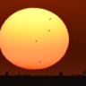 Pigeons fly in front of the sun as it rises over Kuwait City on August 23, 2025. 