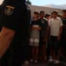 A police officer stands guard as migrant children queue outside a police station to be registered following mass crossings by migrants on foot and by sea from Morocco into Spanish territory, in Ceuta, Spain, August 6, 2026. 