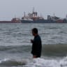 A person wades in the water as ships are seen anchored in the Strait of Hormuz on August 10, 2026 off the coast of Bandar Abbas, Iran. 