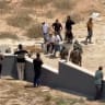 Palestinians use their phones as Israeli settlers and military personnel stand outside a Palestinian home in Qusra, in the West Bank, August 15, 2026, in this screen grab obtained from a video.