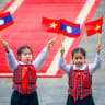 Children wave flags of Vietnam and Laos ahead a welcoming ceremony at the presidential palace in Hanoi on January 26, 2026. 