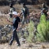 Loui Ridi, a Palestinian-American whose house has been besieged by settlers for over a week, films his property as Israeli soldiers walk on the road behind him, in Kusra, West Bank, August 18, 2026. 
