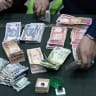 Iraqi dinar and US dollar banknotes are laid out on a table as members of the Shia Muslim community arrive at a centre in Iraq's southern city of Basra accepting charity donations to aid people affected by the ongoing war in Iran and Lebanon