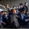 Police officers stand by as ultra-Orthodox men block a road during a protest against conscription into the IDF in Bnei Brak in August.
