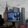 Men sit in front of an advertising board promoting military service under contract in the Russian Armed Forces and informing about payments, against the skyline of downtown Moscow, Russia, August 27, 2026.