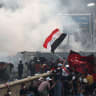 Iraqi anti-government protesters take cover from security forces firing tear gas to keep demonstrators from storming the Green Zone, which hosts government offices and foreign offices, on October 28, 2019 in Baghdad. 