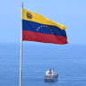 A Venezuelan flag waves as a cargo ship sails at La Guaira Port, Venezuela on August 22, 2026. The Venezuelan Parliament announced an investigation into opposition lawmaker Antonio Ecarri on August 22, 2026, and removed him from his legislative post after he proposed dollarizing the economy.