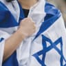 An individual clothed in an Israeli flag recites the Yom Kippur vidui prayer, beating their chest. 