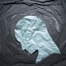 Illustrative image of a head, made of crumpled paper, looking down on a black background. 