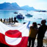 Bystanders display a flag of Greenland as European Commission President Ursula von der Leyen (back L), Greenland's Prime Minister Jens-Frederik Nielsen (back R) and Denmark's Prime Minister Mette Frederiksen visit Qoornoq, September 9, 2026.