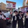 Yehonatan Ovadia, left, holds a Palestinian flag while participating in an anti-Israel protest alongside other anti-Zionist Hasidic Jews who are holding signs from the Neturei Karta group.