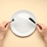 Man with cutlery and plate on beige background.
