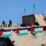 Hamas terrorists stand on a rooftop overlooking a damaged site, in Gaza, February 15, 2025