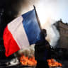 A protester waving a French national flag walks past a fire during clashes prior to the start of a demonstration to protest against the "high cost of living", in Marseille, southern France, on October 17, 2026.