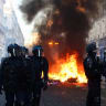 A fire burns, as Police officers in riot gear stand guard, during civil unrest, the day after a national day of demonstrations against the cost of living and rising fuel prices, in Paris, France, October 18, 2026. 