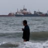 A person wades in the water as ships are seen anchored in the Strait of Hormuz on August 10, 2026 off the coast of Bandar Abbas, Iran.