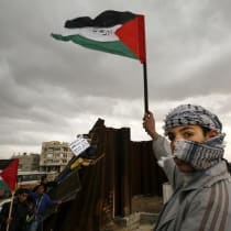 A Palestinian waves a flag near a destroyed section of the border wall between the Gaza Strip and Egypt