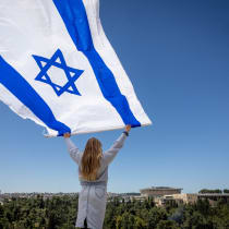 A woman waves a large Israeli flag as people watch the military airshow as part of Israel's 75th Independence Day celebrations, in Jerusalem, April 26, 2023. 