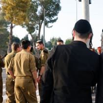  Hombres haredíes vestidos con atuendos ultraortodoxos tradicionales detrás de un grupo de soldados religiosos de las FDI.