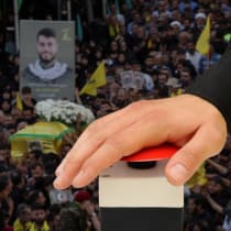  Un "botón rojo" siendo pulsado tras el fondo de un funeral de Hezbolá tras los atentados con artefactos explosivos ocurridos en todo el Líbano (Ilustrativo)