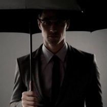  Un hombre misterioso con traje negro, de pie entre las sombras bajo un paraguas, con aspecto de espía o agente secreto [Ilustrativo].
