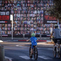  Personas montan en bicicleta en Yom Kippur, frente a un muro con carteles de rehenes, en Jerusalén, el 12 de octubre de 2024 