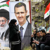  Portraits of ousted Syria's President Bashar al-Assad (R) and Iran's supreme leader Ayatollah Ali Khamenei stand as Palestinians sit at the entrance of the Yarmuk camp for Palestinian refugees, south of Damascus, on March 26, 2024. 