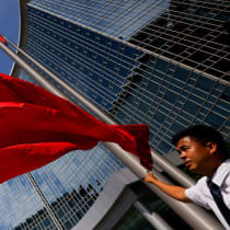 Un empleado de un centro de negocios observa cómo se iza la bandera nacional china, en Pekín, China, el 26 de agosto de 2025.